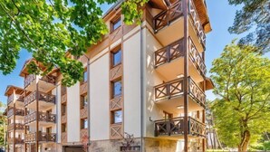 Un hotel de varios pisos con balcones, fachada de piedra y un área de entrada pavimentada.