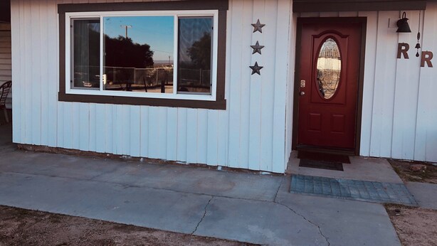 A small, single-story building with a red door, white siding, and a window with a black frame. There are three stars on the wall above the door. - Vacation with the Horses in our Ranch House! Right off Hwy 395 (Inyokern)
