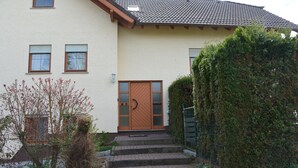 A two-story house with a brown door, a small porch, and a brick pathway leading to the entrance.
