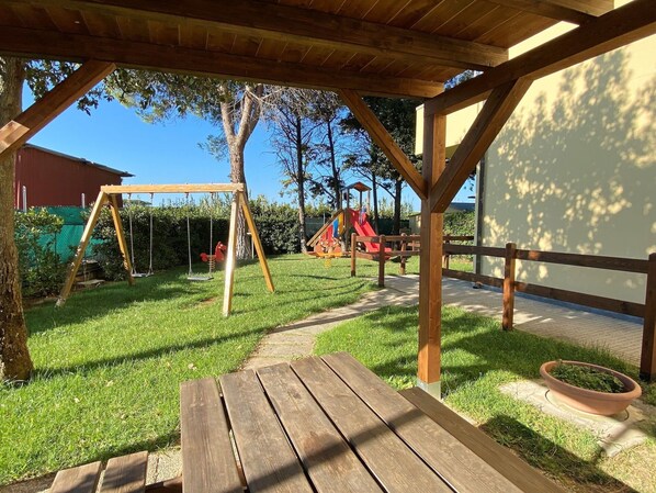 A wooden swing set, a slide, and a picnic table in a grassy outdoor area.