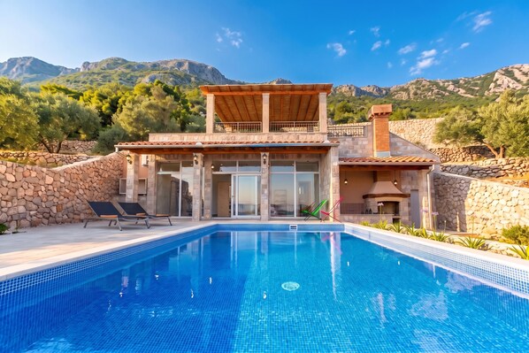 A two-story building with a swimming pool, stone walls, and a view of mountains.