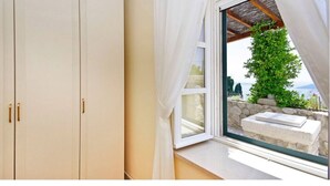 Une pièce dotée d’une grande fenêtre, d’une armoire blanche et offrant une vue sur la verdure et une structure en pierre à l’extérieur.