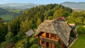 Une cabane en bois, dotée d’un toit en pente, entourée d’une forêt dense et avec des montagnes en arrière-plan.