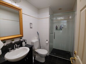 Features a large mirror, glass-enclosed shower, and a white toilet.