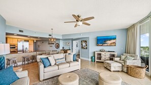 A spacious living area with a large sofa, ottomans, and a dining area with a kitchen in the background.
