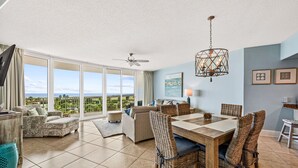 A spacious living area with a dining table, wicker chairs, and a ceiling fan.