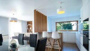 Une cuisine moderne dotée d’un grand îlot central, de meubles blancs et d’une fenêtre donnant sur un jardin.