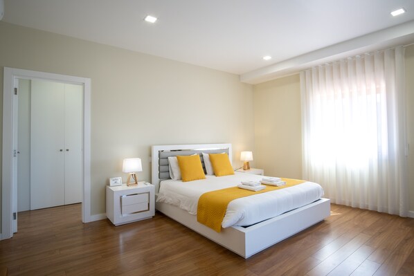 Un dormitorio moderno con una cama grande, mesitas de noche y un ventanal con cortinas.