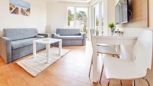 A modern living room with a grey sofa, a white coffee table, and a dining area with a white table and chairs.