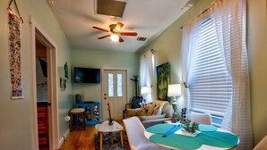 A living room with a ceiling fan, a dining table with chairs, a sofa, and a TV mounted on the wall.