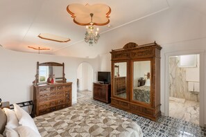 A bedroom with a large bed, a wooden wardrobe, a television, and a chandelier.