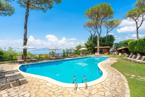 Ein Swimmingpool mit Liegestühlen und Sonnenschirmen, umgeben von Steinfliesen und Bäumen.