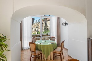A dining area with a round table, chairs, and a view of a stone wall and greenery outside. - MyExclusiveItaly - Elegant Sorrento Coast Villa with Pool&TennisCourt (Massa Lubrense)