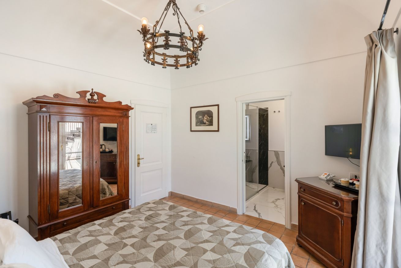 A bedroom with a bed, wardrobe, chandelier, television, and a door leading to a bathroom.