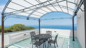 Un área de estar al aire libre techada con mesa y sillas, con vistas a un paisaje pintoresco.