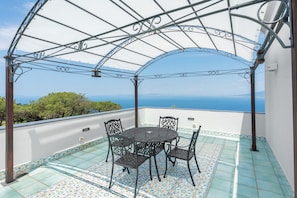 A covered outdoor seating area with a table and chairs, overlooking a scenic view.