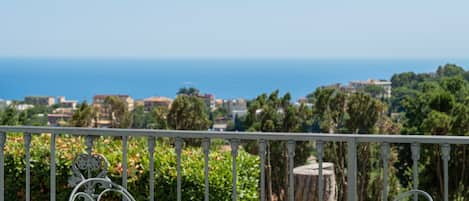 A balcony with a metal railing, a small round table, and a view of the sea and distant buildings.