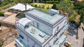 Un edificio de varios pisos con piscina en la azotea, zona de estar al aire libre y cancha de tenis.