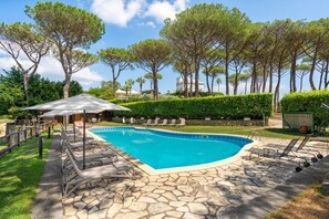 A swimming pool with a stone deck, surrounded by lounge chairs and a covered seating area.