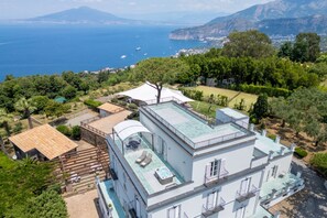 A multi-story building with a rooftop terrace, a swimming pool, and a view of the sea.