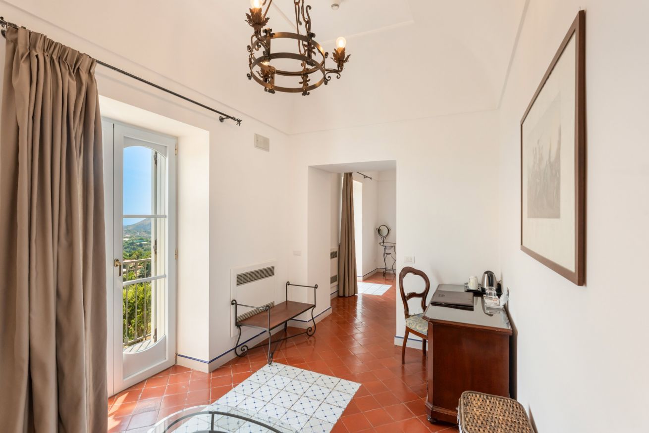 A spacious room with a large window, a desk, a chair, and a chandelier.