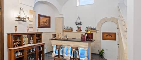 Zona de bar con taburetes, barra y estanterías llenas de botellas.