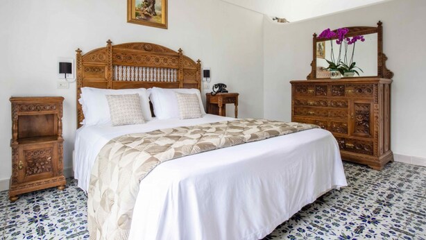 A bedroom with a large wooden bed, a wooden dresser, and a mirror with flowers.