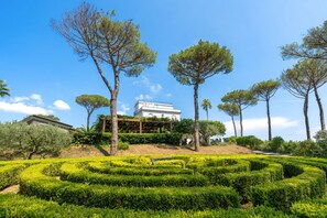 Ein angelegter Garten mit einem weißen Gebäude, Bäumen und einem Labyrinth.