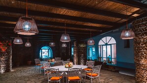 An outdoor dining area with a round table and chairs, surrounded by stone flooring and decorative lighting fixtures.