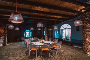 Un área de comedor al aire libre con una mesa redonda y sillas, rodeada de suelo de piedra y luminarias decorativas.