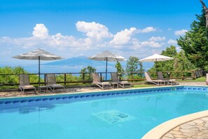 A swimming pool with lounge chairs and umbrellas, surrounded by a stone deck and a view of a mountain range.