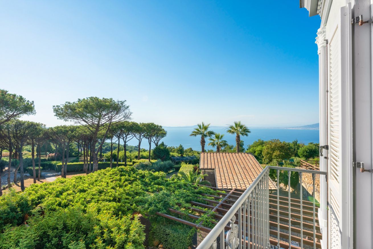 A balcony with a view of a landscaped garden and the sea.