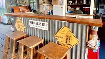 Een rustieke bar met houten krukken en een golfplaten achtergrond, met borden zoals 'Old Farts Bar' en 'Dunny Outback 50 Metres'.