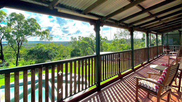 Una terraza cubierta al aire libre con barandas de madera y sillas, con vistas a un paisaje verde y exuberante.