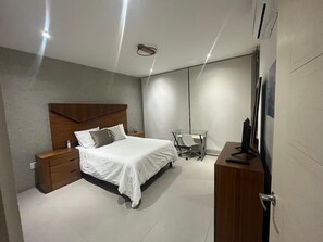 Une chambre à coucher moderne comprenant un lit, une table de chevet, un bureau, une chaise et un téléviseur posé sur un meuble en bois.