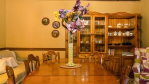 Ein Esszimmer mit Holztisch, Stühlen, einer Blumenvase, einem Schrank mit Geschirr und einem gepolsterten Sessel.