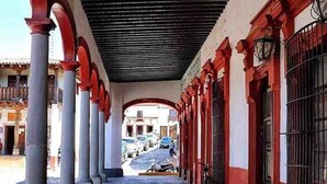 Un corredor cubierto con columnas y arcos, que conduce a un edificio con ventanas de celosía.
