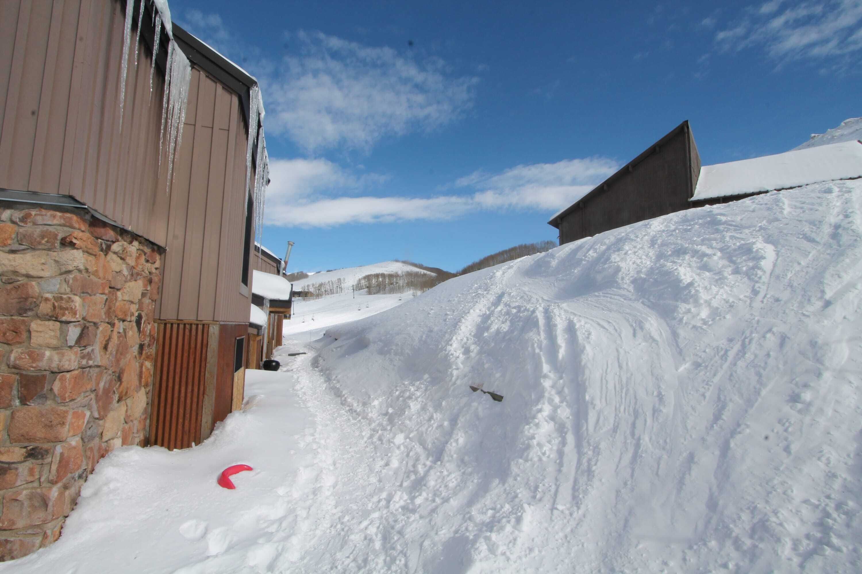 A snow-covered path leading to a building with a stone wall and wooden siding.