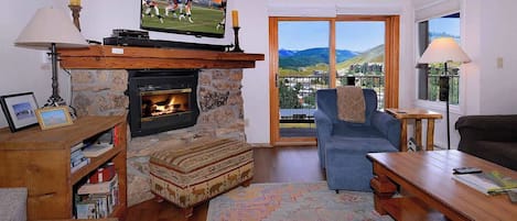 A living room with a fireplace, a television, a sofa, and a view of the outdoors.