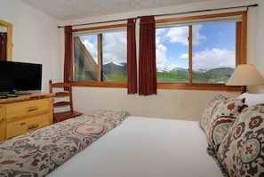 Um quarto com cama, cômoda de madeira, televisão e janela com cortinas.