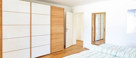 A bedroom with a bed, a wardrobe, a mirror, and a door leading to another room.