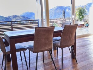 A dining area with a wooden table and chairs, large windows with a mountain view, and a wooden floor. - Bergblick Acht, Österreich (Innerschwand am Mondsee)