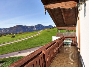 A balcony with a view of a green field and mountains.