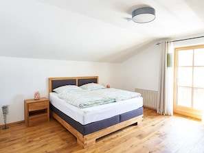 A bedroom with a wooden bed, a nightstand, a radiator, and a window with curtains. - Bergblick Acht, Österreich (Innerschwand am Mondsee)