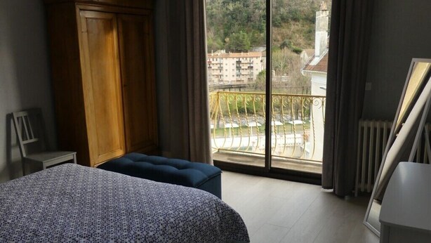 Un dormitorio con una cama grande, un armario de madera y un balcón con vistas a edificios y vegetación.