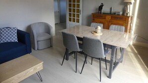 Un área de comedor con una mesa de mármol y cuatro sillas, un sofá azul y un aparador de madera con una lámpara.