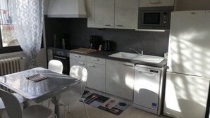Una cocina moderna con microondas, cafetera y lavavajillas. Hay una mesa de comedor con sillas y una ventana con cortina.