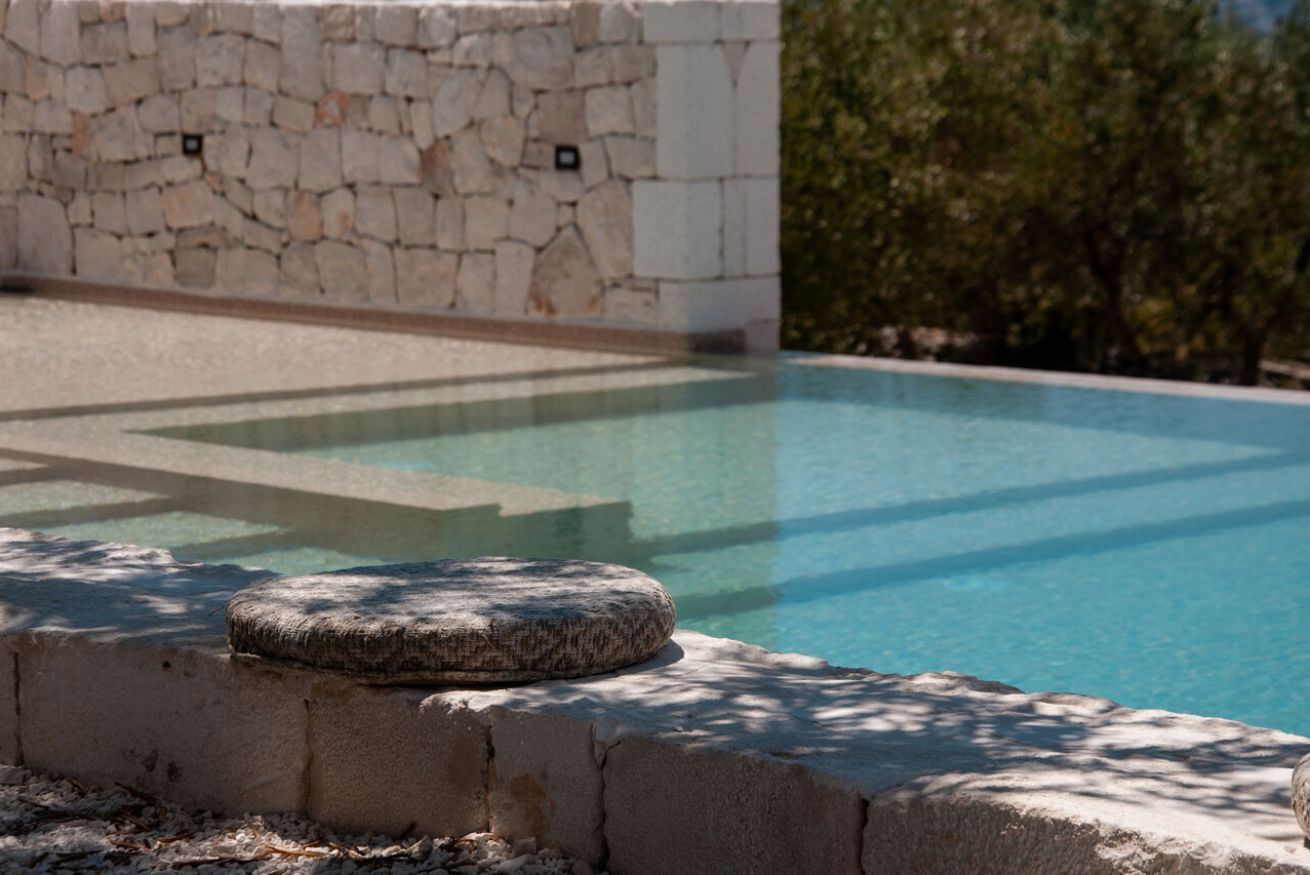 Une piscine avec un mur en pierre et un élément décoratif circulaire en pierre au premier plan.
