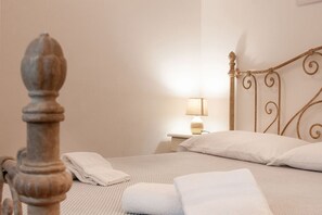 A neatly made bed with white linens, a bedside lamp, and a wooden headboard.