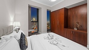 A hotel room with a bed, a nightstand, a lamp, a wardrobe, and a view of the city at night. - FIRST CLASS | 3BR | Burj Khalifa & Fountain view (Downtown)